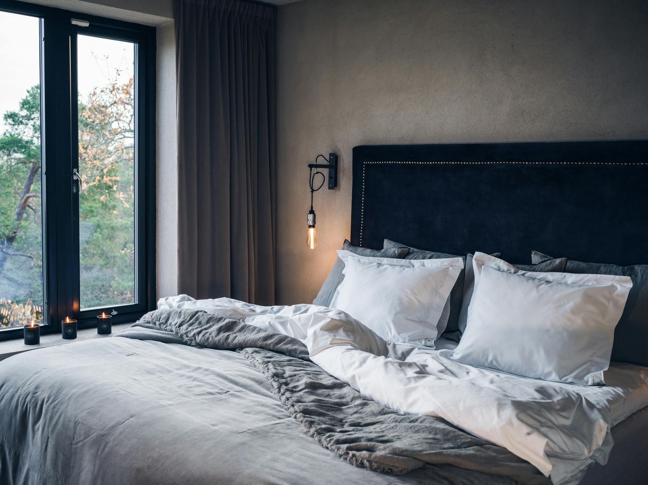 Bett mit weißer und grauer Bettwäsche von Spirit of the Nomad. Im Hintergrund Kerzen