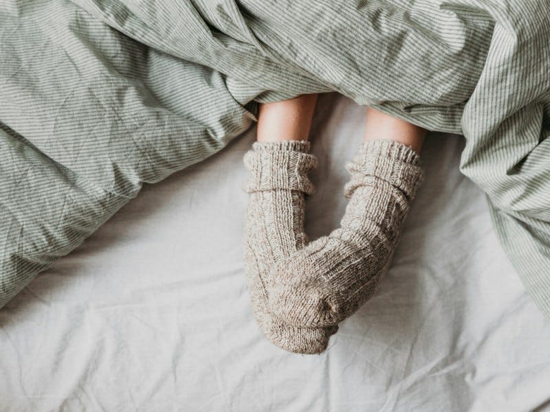 Füße mit Wollsocken unter gestreifter Bettdecke