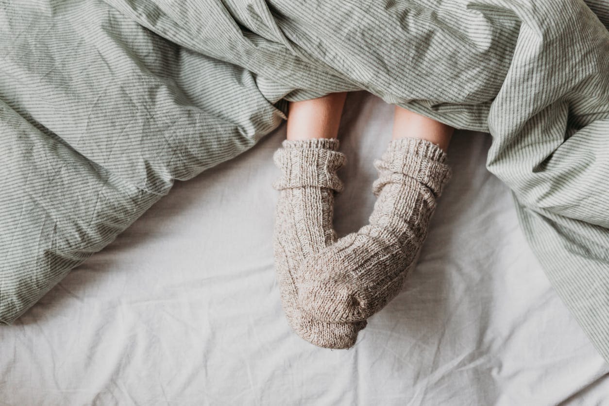 Füße mit Wollsocken unter gestreifter Bettdecke