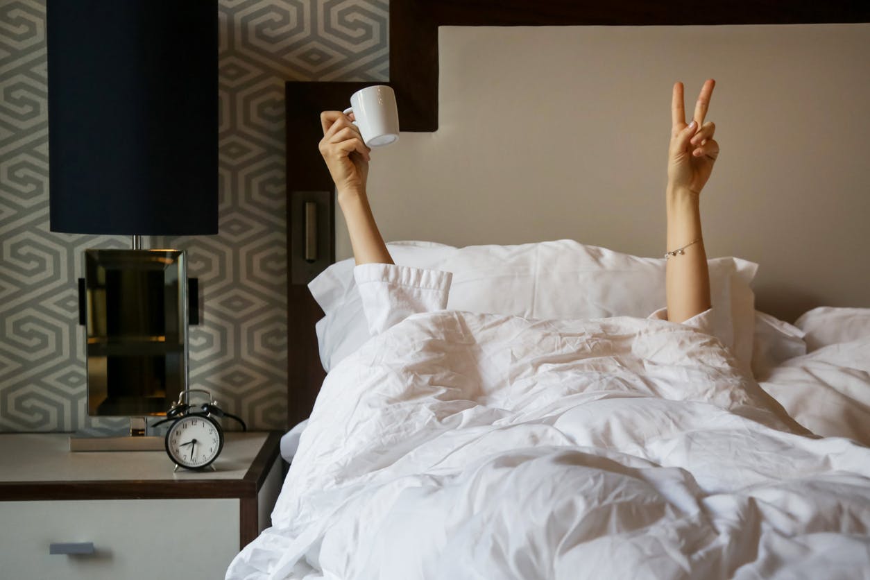 Frau mit Kaffeetasse im Bett zeigt ein Handzeichen